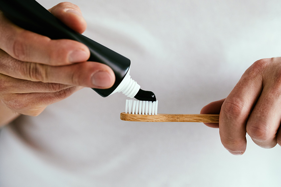 Un homme met du dentifrice à base de charbon sur sa brosse à dents